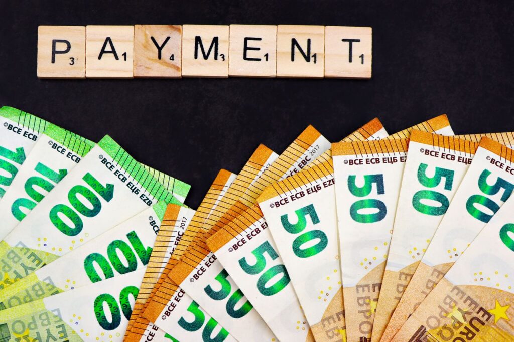 Euro banknotes fanned out with 'PAYMENT' spelled in Scrabble tiles, representing finance and commerce.